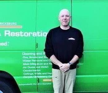 Male employee standing outside with no hair in front of green background