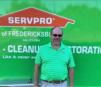 Male owner of company with medium brown hair standing in front of green SERVPRO van